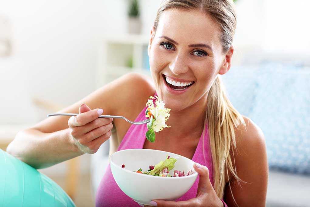 604342055 Woman smiling and eating a salad bowl