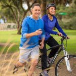 A couple enjoying outdoor exercise with one riding a bike and the other jogging alongside