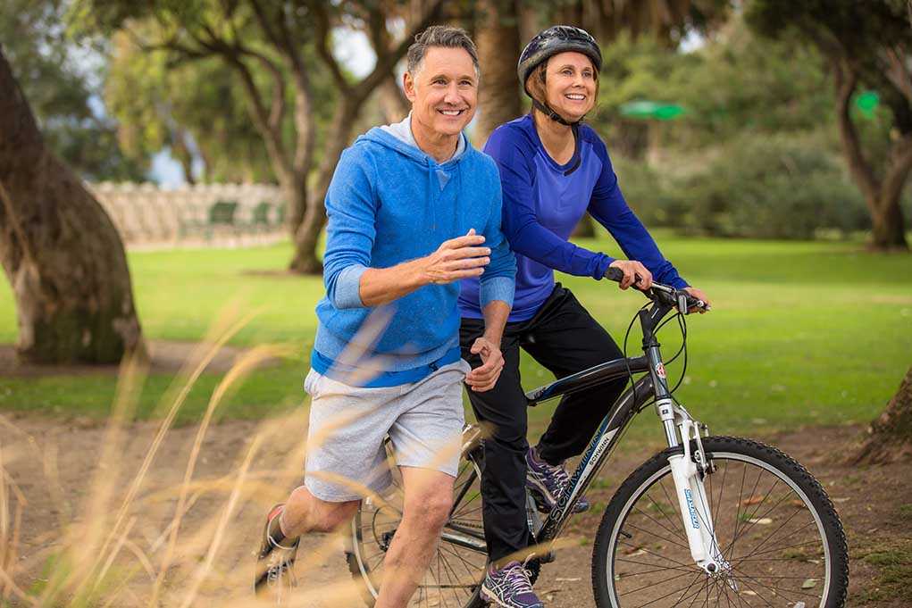 shutterstock_232027741.jpg A couple enjoying outdoor exercise with one riding a bike and the other jogging alongside