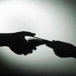 Silhouette of hands exchanging money in dim light