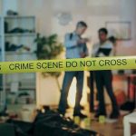 Crime scene with tape and investigators examining evidence.