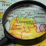 Magnifying glass focusing on Venezuela and Colombia on map.