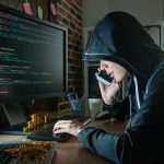 Hacker in hood using computer and phone analyzing code