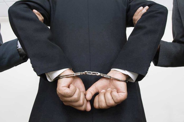 121141399 Person handcuffed in suit, escorted by two others.