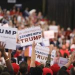 TRUMP’S Grip Tightens: Primaries Prove His Power Crowd holding signs supporting Trump at a rally.