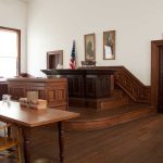 Judge’s Chambers Affair with Police Officer EXPOSED! Interior of a historic courtroom with wooden furniture and an American flag