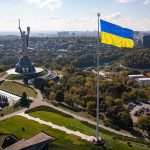 Putin Pressure PlayâWhy Timing Matters Large Ukraine flag with cityscape in background.