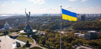 Putin Pressure Play—Why Timing Matters Large Ukraine flag with cityscape in background.