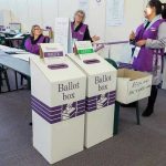 California Vote Delays Spark Debate Election polling station with ballot boxes and officials.