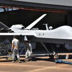 Military drone being serviced by ground crew outside a hangar