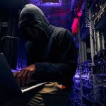 Hooded person using a laptop in a dark server room