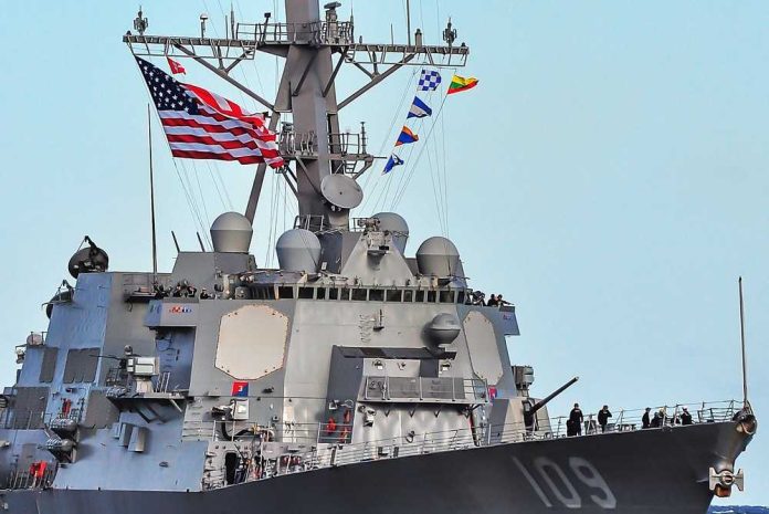 shutterstock_2743496331-1 A naval destroyer displaying the American flag and various signal flags