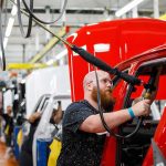 Factory Visit Sparks Big Economic Debate Worker assembles red vehicle on factory line