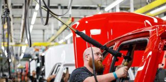 Factory Visit Sparks Big Economic Debate Worker assembles red vehicle on factory line