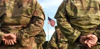 Supreme Court Allows Parts of Troop Ban Soldiers in camouflage stand with hands behind backs facing a U.S. flag
