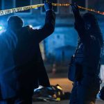 Investigators at night lifting police tape at a crime scene