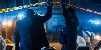 Investigators at night lifting police tape at a crime scene