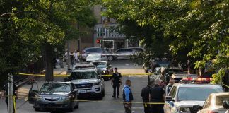 The 911 Call Is Out. The Killer Isn’t. Police officers secure a residential street with patrol cars and yellow tape