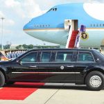 Presidential limousine beside a large blue-and-white jet on a runway