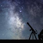 Silhouette of person with telescope under starry Milky Way sky