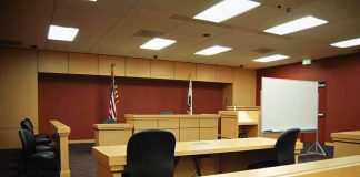 Postal Cop Turns Thief—Elderly Looted Interior view of an empty courtroom with wooden furniture and American flags