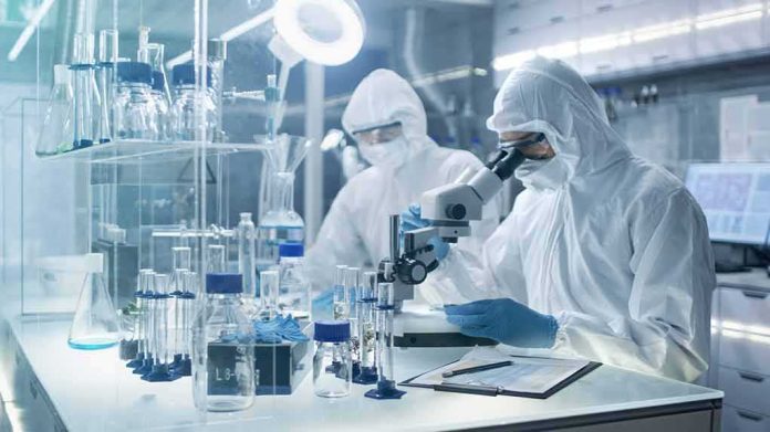 shutterstock_684989614 Scientists in protective suits using a microscope in a laboratory