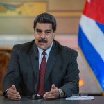 Man speaking at podium with Cuban flag in background.