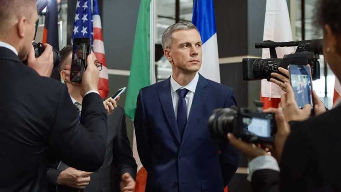 Man in suit surrounded by reporters and cameras