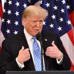 Donald Trump speaking at a podium with American flags behind him