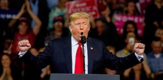 Donald Trump speaking at a rally podium with arms raised