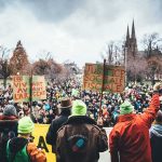 EU’s First Social Ban Ignites Fury Christian Jones at a large outdoor protest with crowds and handmade signs