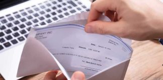 Federal Paid Leave Costs Hit $9.5B Hands opening an envelope with a check near a laptop