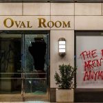 vandalized storefront with broken glass door and red graffiti on window