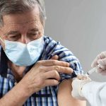 Older man in mask receiving a vaccine injection