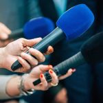 Young Democratic Socialist Defeats Longtime Incumbent Reporters holding colorful microphones