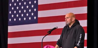 Old Political Dispute Sparks Debate Man in hoodie speaking at a podium before a large U.S. flag