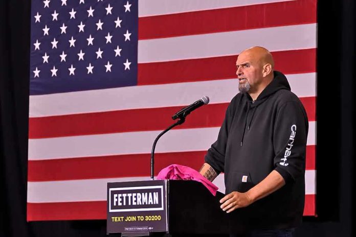 Man in hoodie speaking at a podium before a large U.S. flag