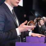 Speaker in suit at podium gesturing during conference