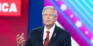 Old Video Fuels New Senate Race Debate Man in suit speaking at a podium on a colorful stage