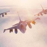 Three fighter jets flying in formation above clouds at sunrise