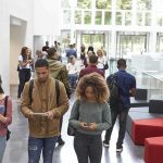 Students walking through a bright campus lobby using mobile devices