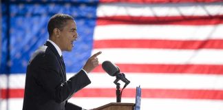 Two-Decade Alliance Shapes the Campaign Speaker at podium with microphones in front of US flag